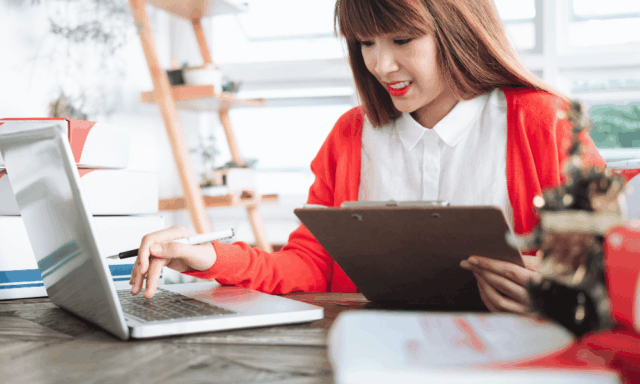 A marketer performs tasks on a laptop while holding a clipboard.