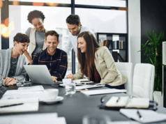 Becoming a Multiskilled Marketer: Resources To Help You Grow A group of marketers in a modern office collaborate around a laptop, smiling as they discuss ideas during a professional training session.