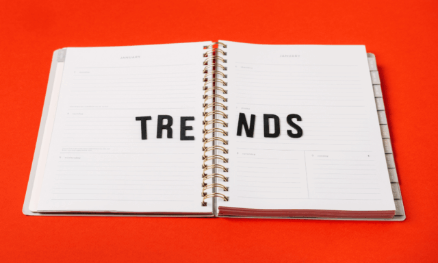 An open planner on a bright red background with the word “TRENDS” spelled across its pages in black letters.